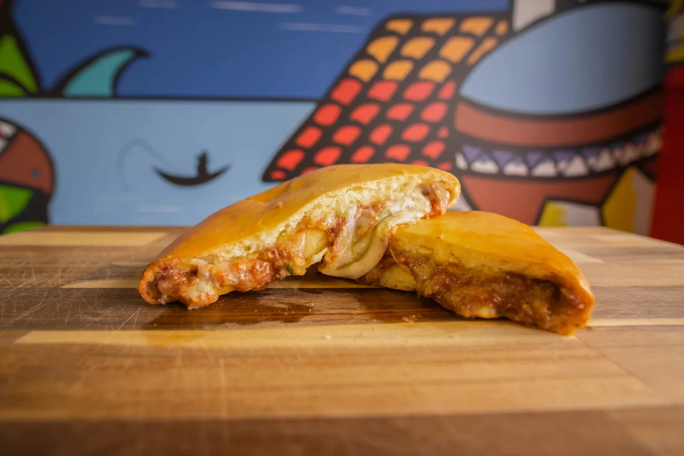 A Donut Pupusa cut open on a wooden board in front of the Winstar mural